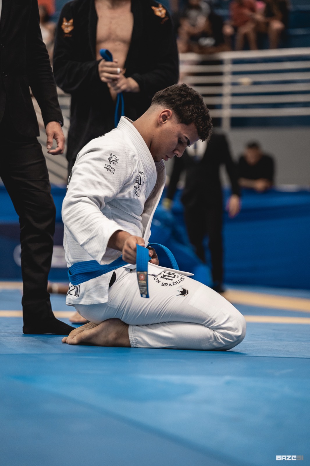 Antonio ajoelhado amarrando a faixa azul no tatame